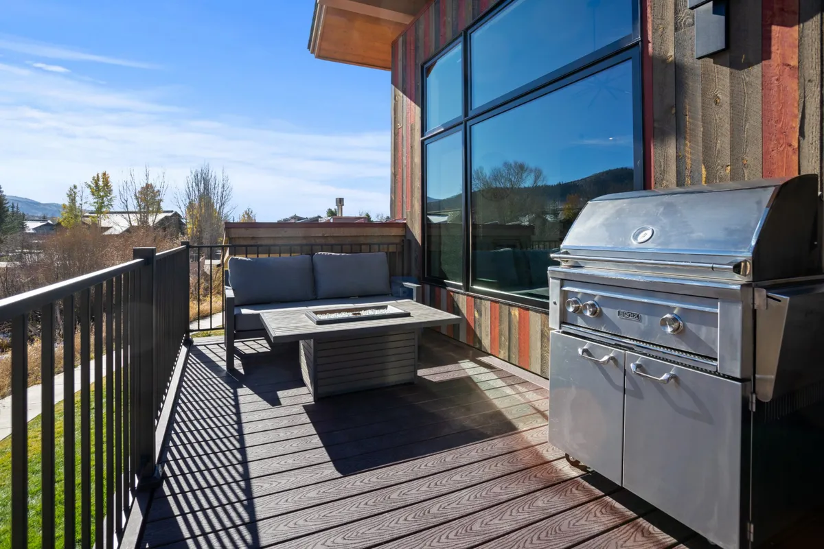 A spacious backyard setup with a barbecue grill, comfortable outdoor seating, a fire pit, and spectacular mountain scenery. The area invites relaxation after an active day, perfect for unwinding or socializing around the fire pit at twilight.