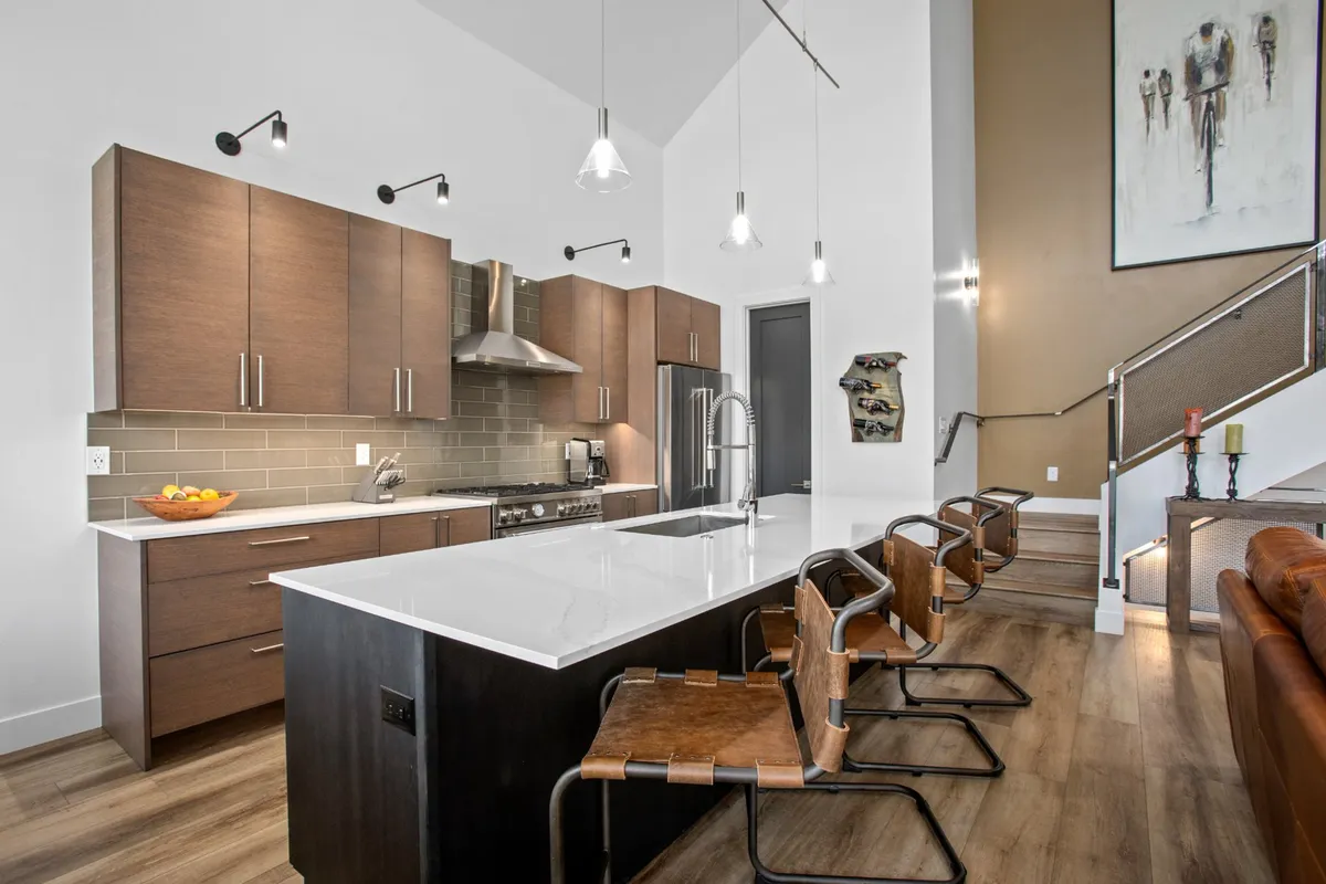 A spacious, contemporary kitchen featuring a large island with bar stools, stainless steel appliances, and modern artwork on the wall. The scene blends functional cooking space with a social setting, perfect for both gourmet preparation and casual dining.