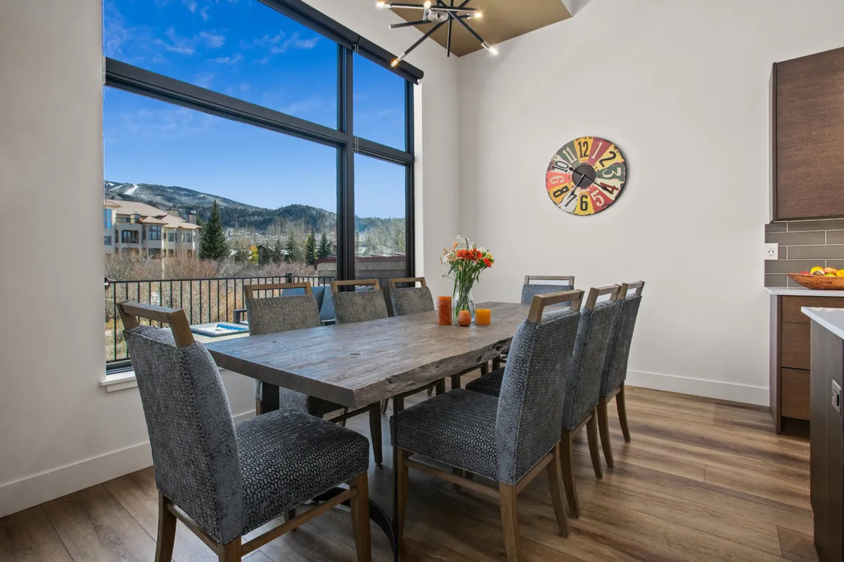 A warm, inviting dining area with a large table, modern light fixture, expansive windows, and a beautiful floral centerpiece. The space is set up for family dinners, celebrations, and cozy gatherings, with natural light flooding the room.
