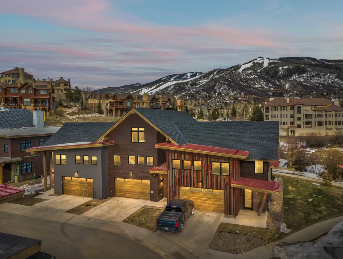 A view of the home's modern architecture set against a mountain backdrop, with illuminated windows hinting at warmth inside. The scene suggests the connection between the home and its natural surroundings, as well as the invitation to explore nearby trails and community amenities.