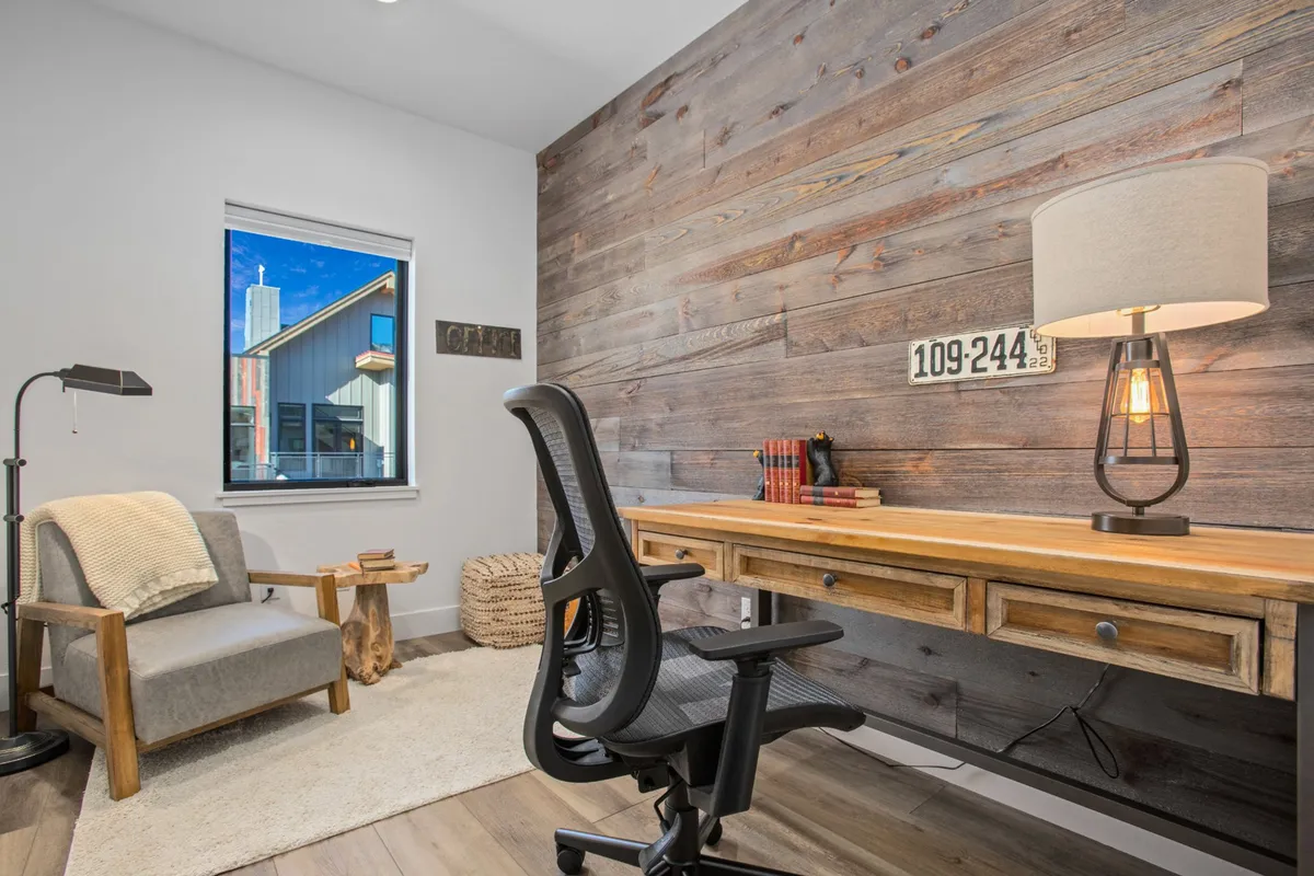 A calm, focused workspace featuring a wooden accent wall, a comfortable desk with a lamp, a cozy chair, and a window offering natural light and a peek outside. The scene feels designed for productivity and relaxation, ideal for remote work or creative projects.