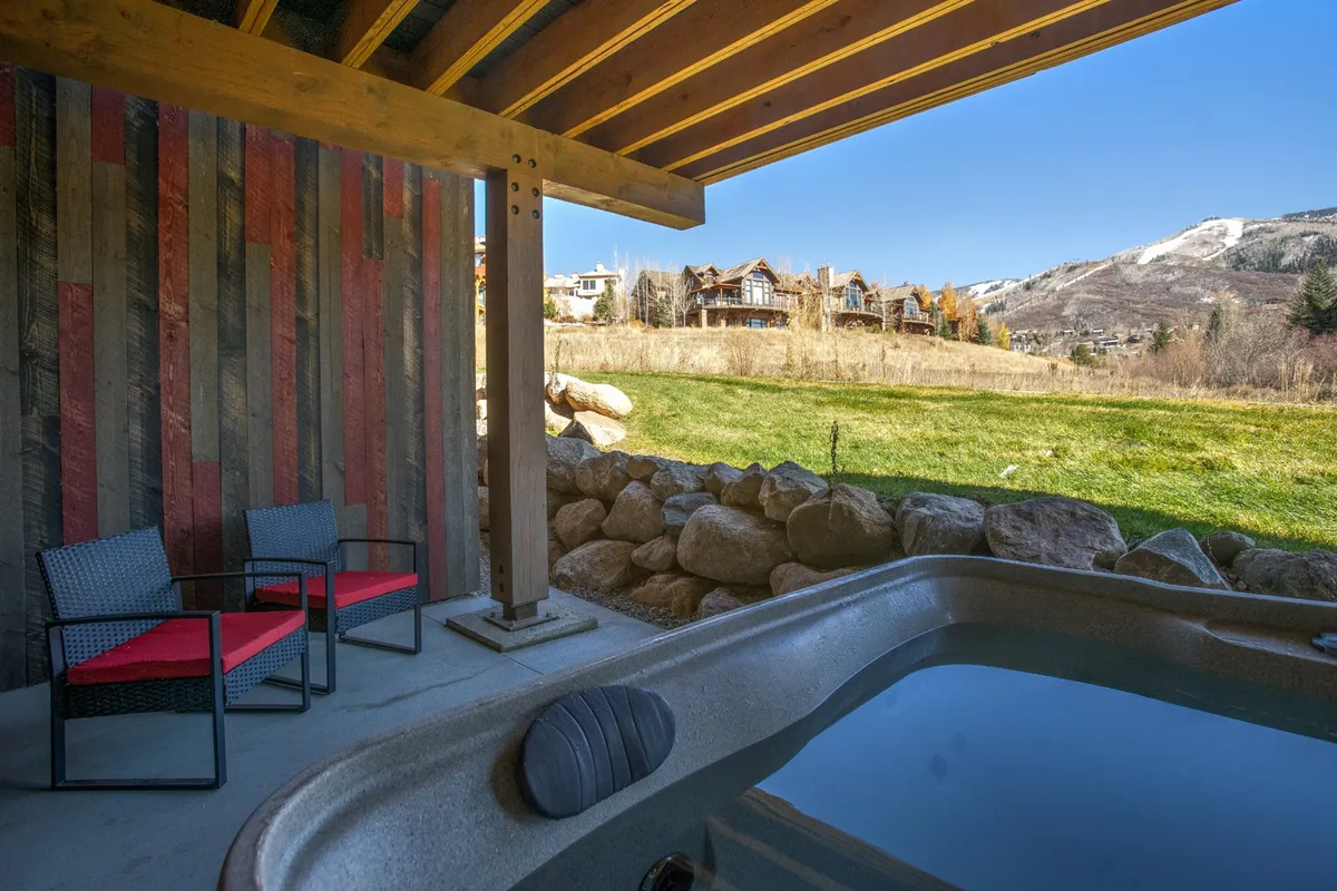An inviting exterior hot tub framed by wooden beams and a rock wall, with outdoor chairs nearby. The setting is tranquil and private, perfect for soaking while enjoying the fresh mountain air and scenic views.